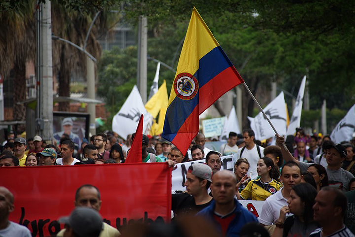 Dezenas de pessoas em uma manifestação carregando bandeiras, entre as quais se destaca uma da Colômbia