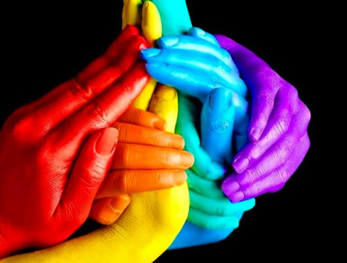 Mãos entrelaçadas nas cores da bandeira LGBTQIA+ com fundo preto