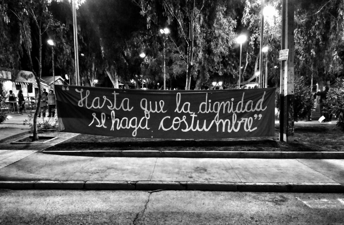 Foto em preto e branco com uma faixa negra ao fundo com a frase, escrita em espanhol, "Até que a dignidade se faça costume"