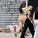 Imagem com morador de rua dormindo sob marquise e pessoas caminhando indiferentes.