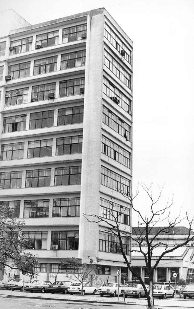 Foto em preto e branco da lateral do prédio da FACED com carros antigos estacionados à frente.