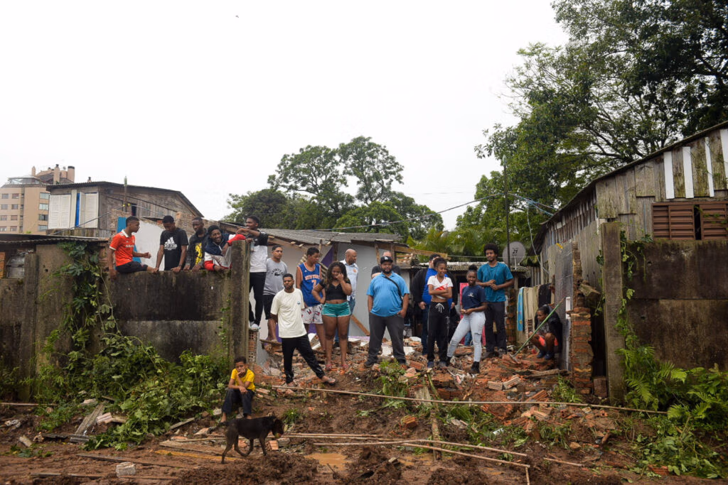 A fotografia mostra moradores do Quilombo Kédi reunidos sobre os escombros de uma casa demolida. |Foto: Alass Derivas / Deriva Jornalismo