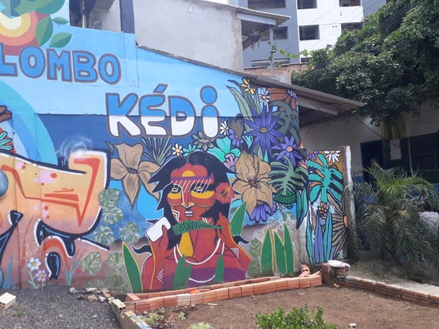 A foto mostra um painel pintado na parede externa de uma casa trazendo o nome Quilombo Kédi, uma pessoa e flores. | Foto: Repórter Popular/reprodução