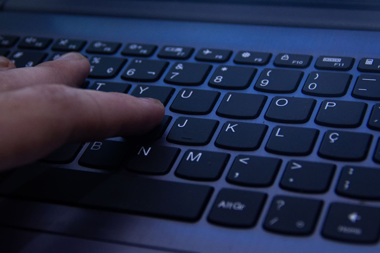 Imagem mostra detalhes de teclado de notebook, com dedos de uma pessoa tocando a tecla 'H'.