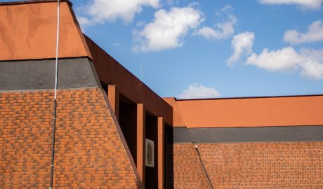 Prédio presente na Faculdade de Educação Física, Fisioterapia e Dança, feito de tijolos alaranjados. No fundo, céu azul em dia ensolarado.