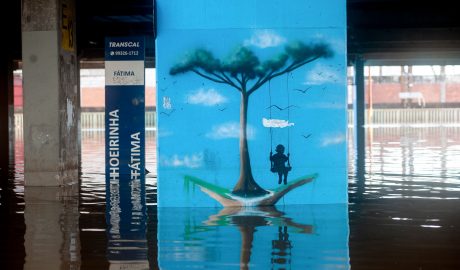 Fotografia mostra grafite representando criança brincando em balanço em parede de terminal rodoviáriário metropolitano, em Porto Alegre, durante a inundação de 2024