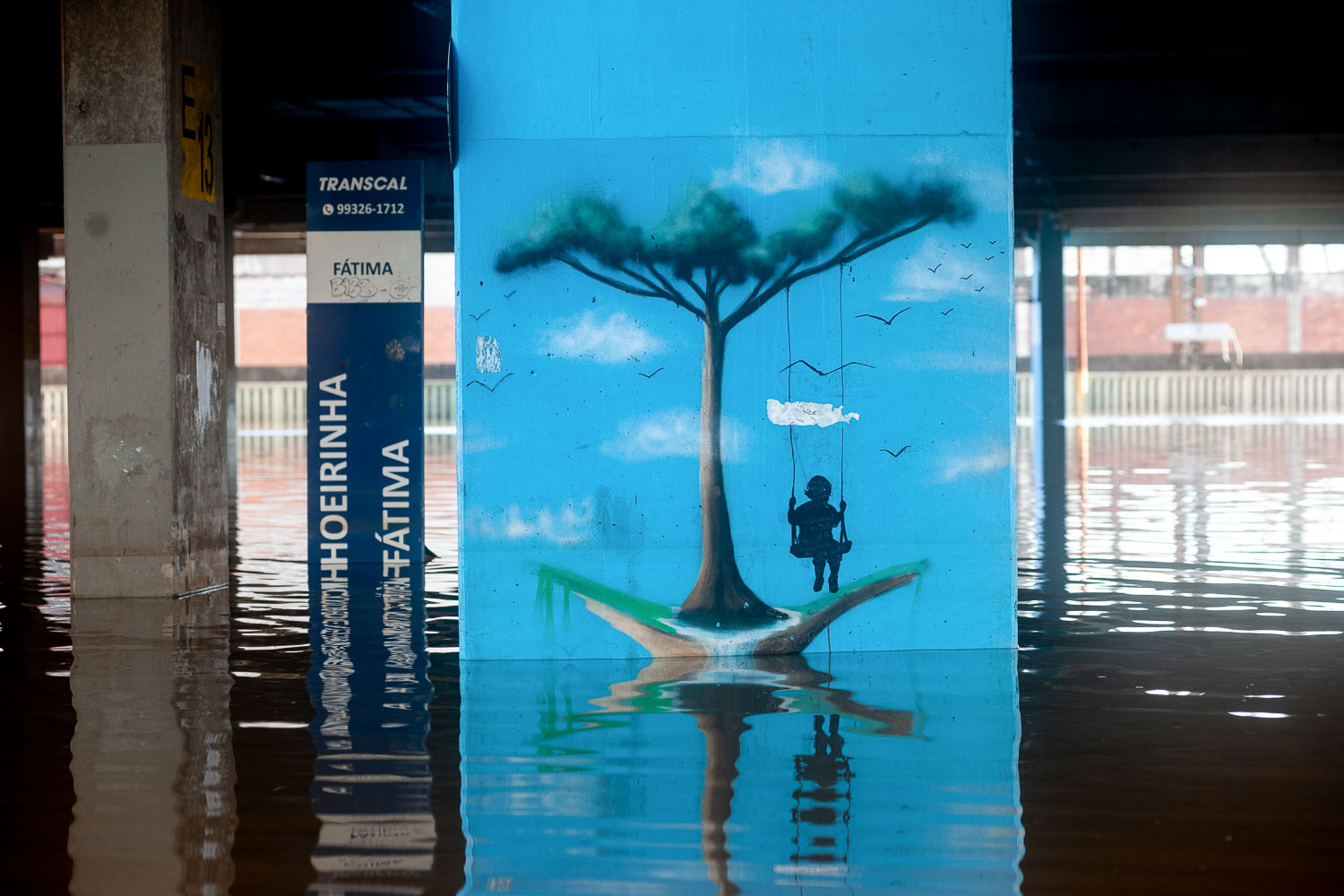 Fotografia mostra grafite representando criança brincando em balanço em parede de terminal rodoviáriário metropolitano, em Porto Alegre, durante a inundação de 2024